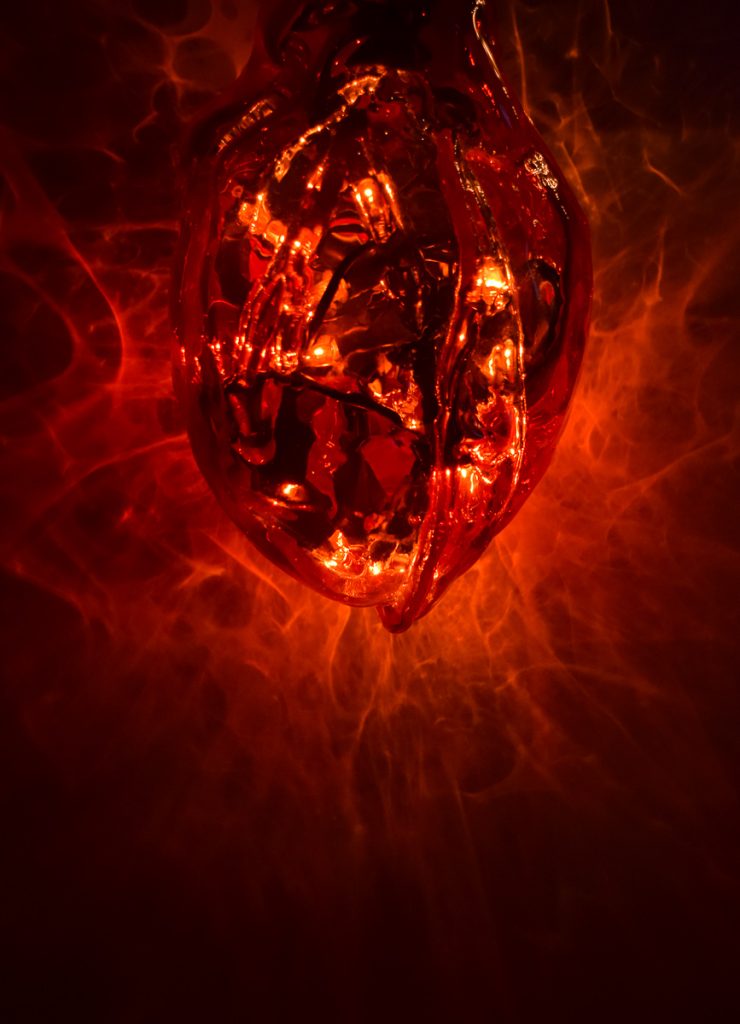 Art piece "The Eternal Debate of the Unconcious Mind" in 2016 by Alise Stopina. Blood red heart shaped blown glass, with heart beat pulsiating red light in them. With light turned on background to show light fractures on the background.
