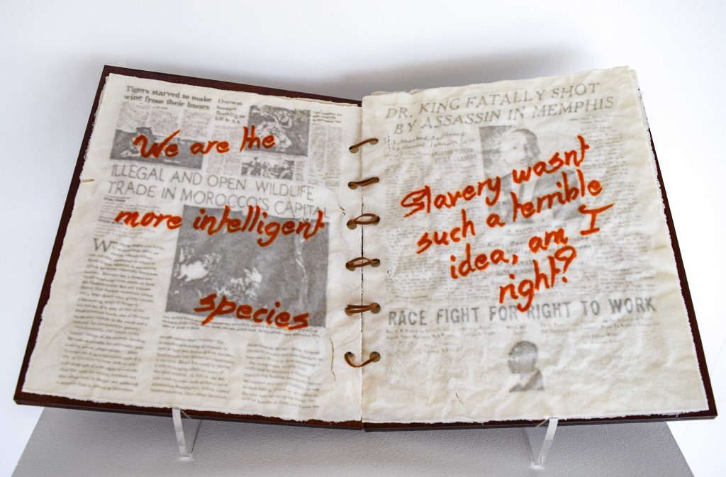 Art piece "Insert Sarcastic Title Here" in 2018 by Alise Stopina. White glass powder with printed text and hand written red satarical quotes. Bound as a book in front view on white background.
