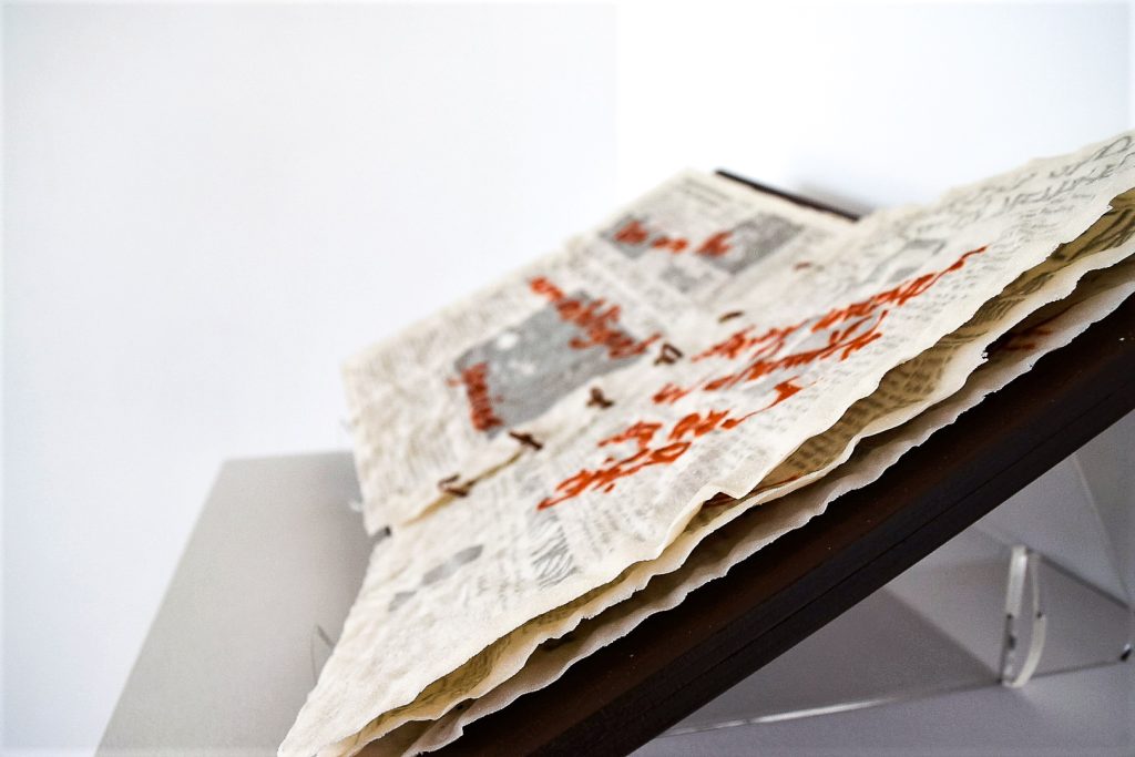 Art piece "Insert Sarcastic Title Here" in 2018 by Alise Stopina. White glass powder with printed text and hand written red satarical quotes. Bound as a book in side view on white background.
