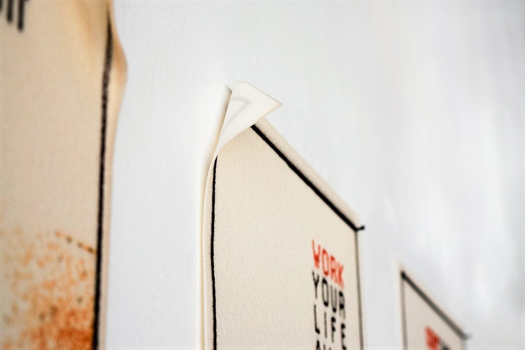 Art piece "Something" in 2018 by Alise Stopina. Paper colored eight glass powder with printed satirical quotes and images related to quotes. Zoomed in detail shot of overall pieces in side angle.
