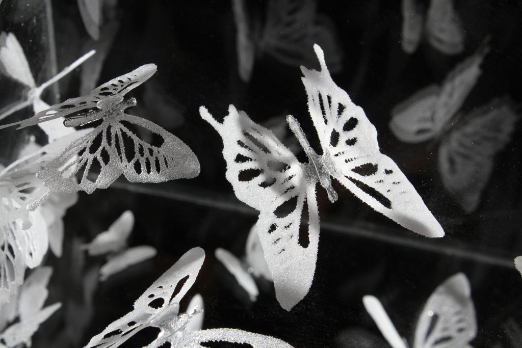 Close up of white powder glass butterflies in a glass vase on a black background by glass artist Alise Stopina